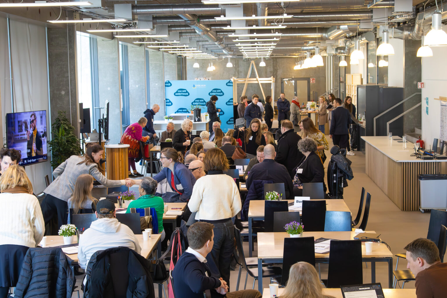 Et stort rum med glasvinduer hvor folk sidder i en forsamling